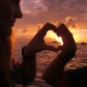 couple form heart hands around luxury catamaran in sunset on island in belize