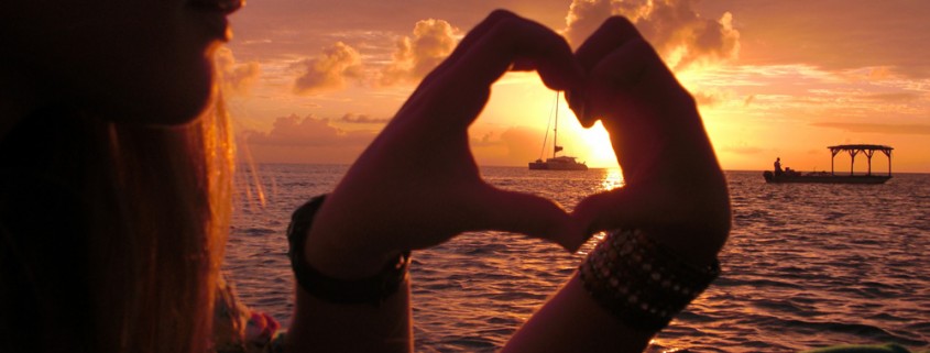 couple form heart hands around luxury catamaran in sunset on island in belize