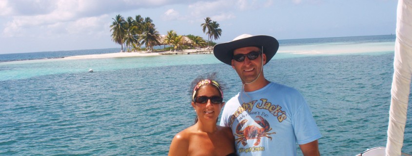 couple possess on catamaran charter with goff's caye island in belize in background