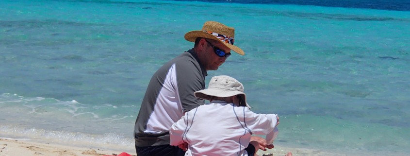 father son playing in white sand beach near the blue green waters of belize