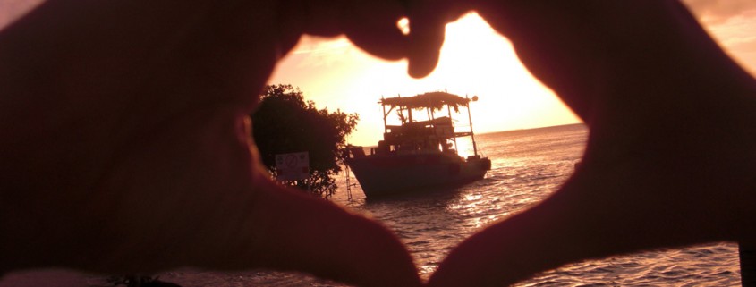 heart hands around boat at sunset near remote island in belize