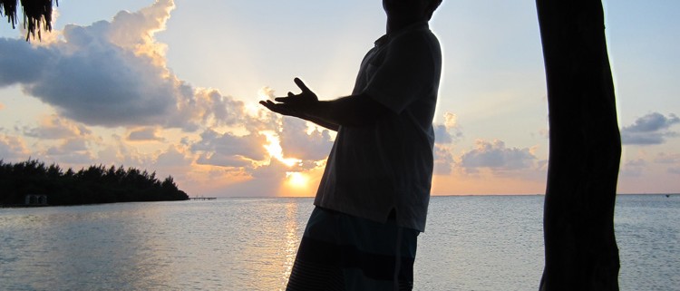 man silhouette pointing to amazing sunset on remote island reef in belize