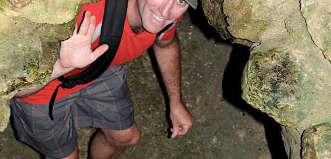 man waves as he climbs through narrow gap in caves belize