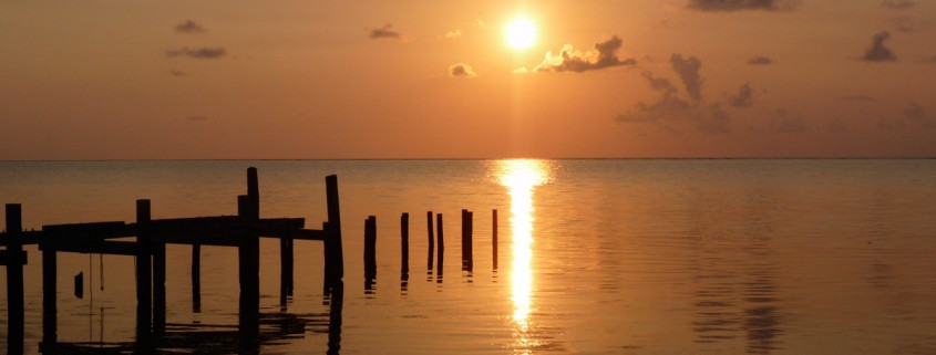 sunset over water and silhouette of dock in belize