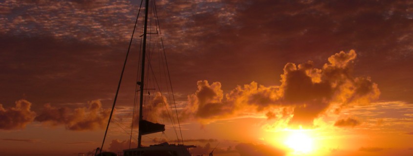 sunset over water in belize with silhouette of luxury yacht chartered for vacation