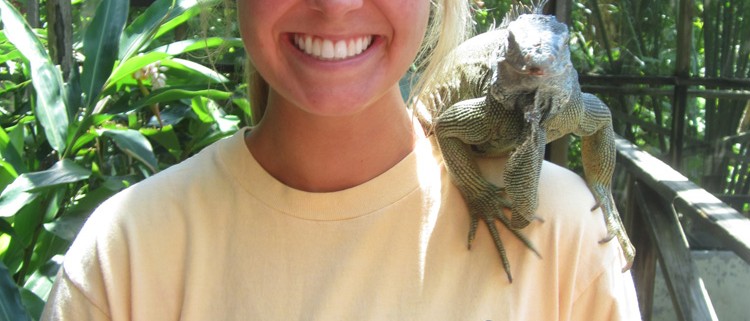 woman poses with large green iguana on shoulder